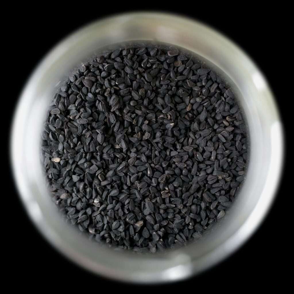 A close-up, top view of black cumin seeds (Nigella sativa) stored in a glass jar.